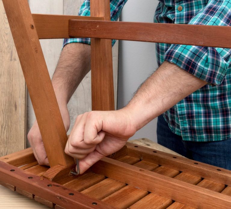 Un homme assemble un tabouret en bois avec des outils à la main.