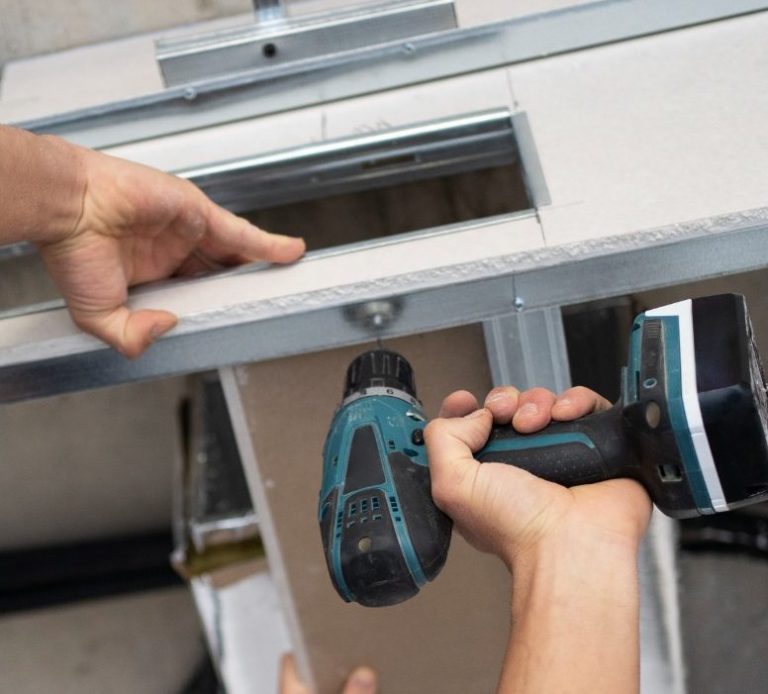 Main d'une personne tenant une perceuse électrique, travaillant sur une structure en métal.